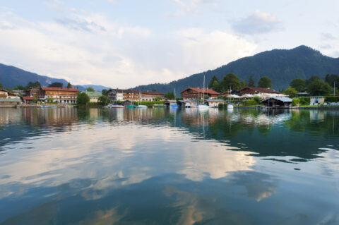 Sommerlicher Tegernsee mit vorbeifahrenden Schiffen, charmanten Häusern am Ufer und beeindruckendem Alpenpanorama – Urlaubsidylle nahe dem Relais Chalet Wilhelmy in Bad Wiessee